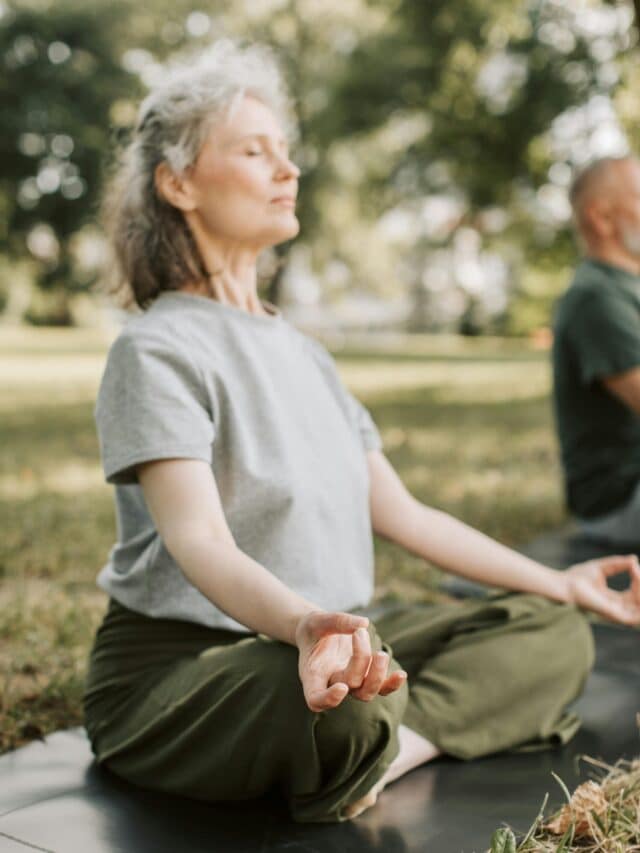 Elderly woman practicing meditation on a yoga mat in a serene outdoor setting.